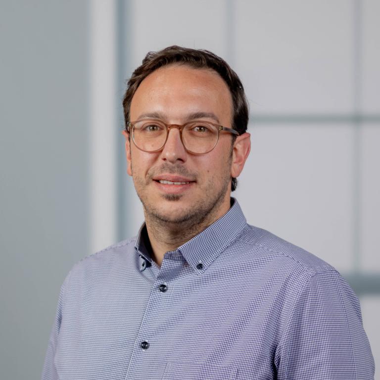Porträtfoto eines Mannes mit Brille und blauem Hemd vor hellem Hintergrund